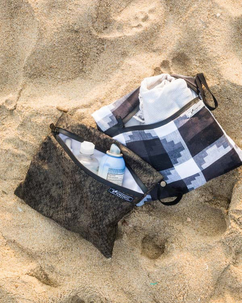 Reusable Wet Bags NZ on sandy beach holding toiletries and clothes. Eco-friendly waterproof bags for swimming, travel, and zero-waste living.